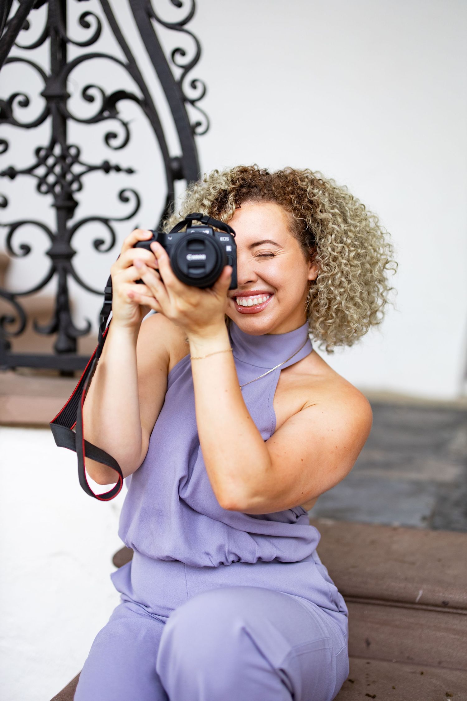 Photographer in lavender outfit smiling while taking pictures with professional camera.
