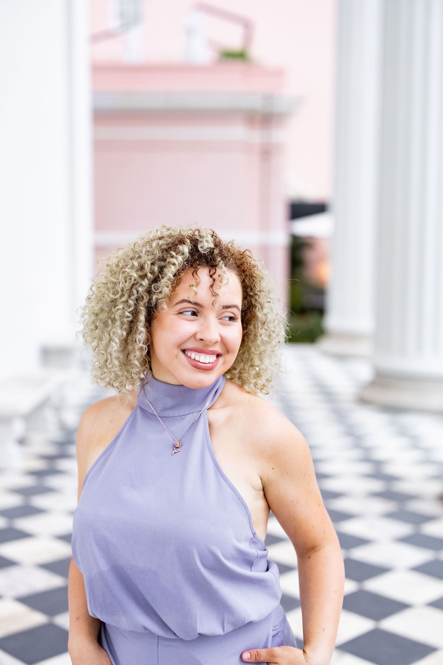 Woman in a lavender halter dress smiling while standing in front of a classical building with columns.