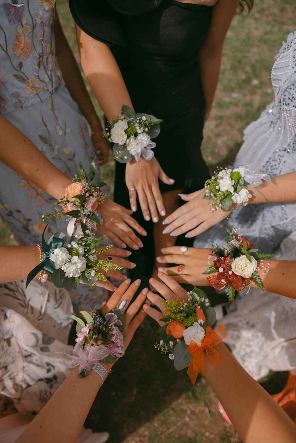 Bridesmaids showing their wrists with delicate floral corsages arranged in a circle.