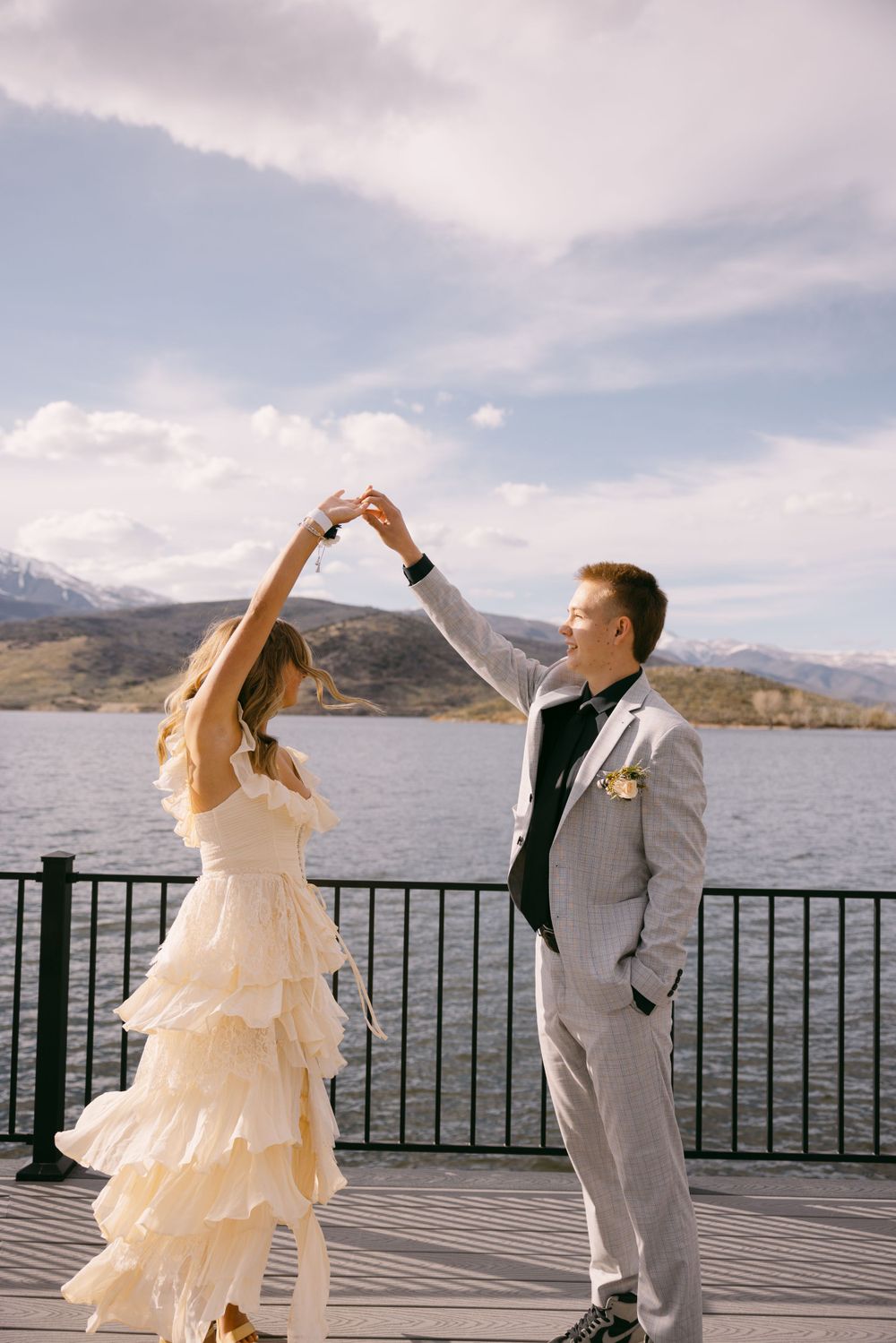 A couple dances together on a lakeside deck with mountains in the background.