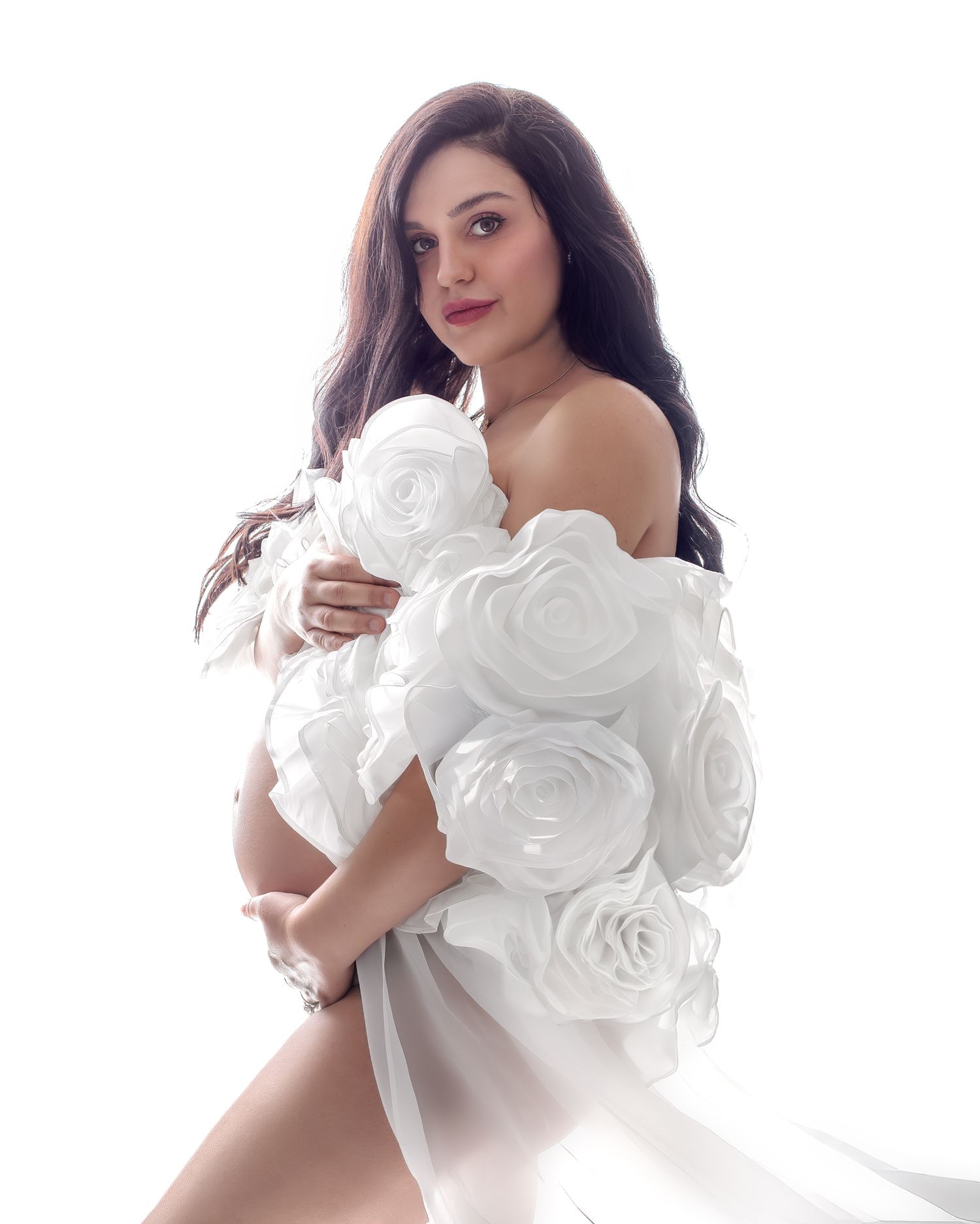 Pregnant woman in a white rose cape against a backlit glowing white light backdrop.