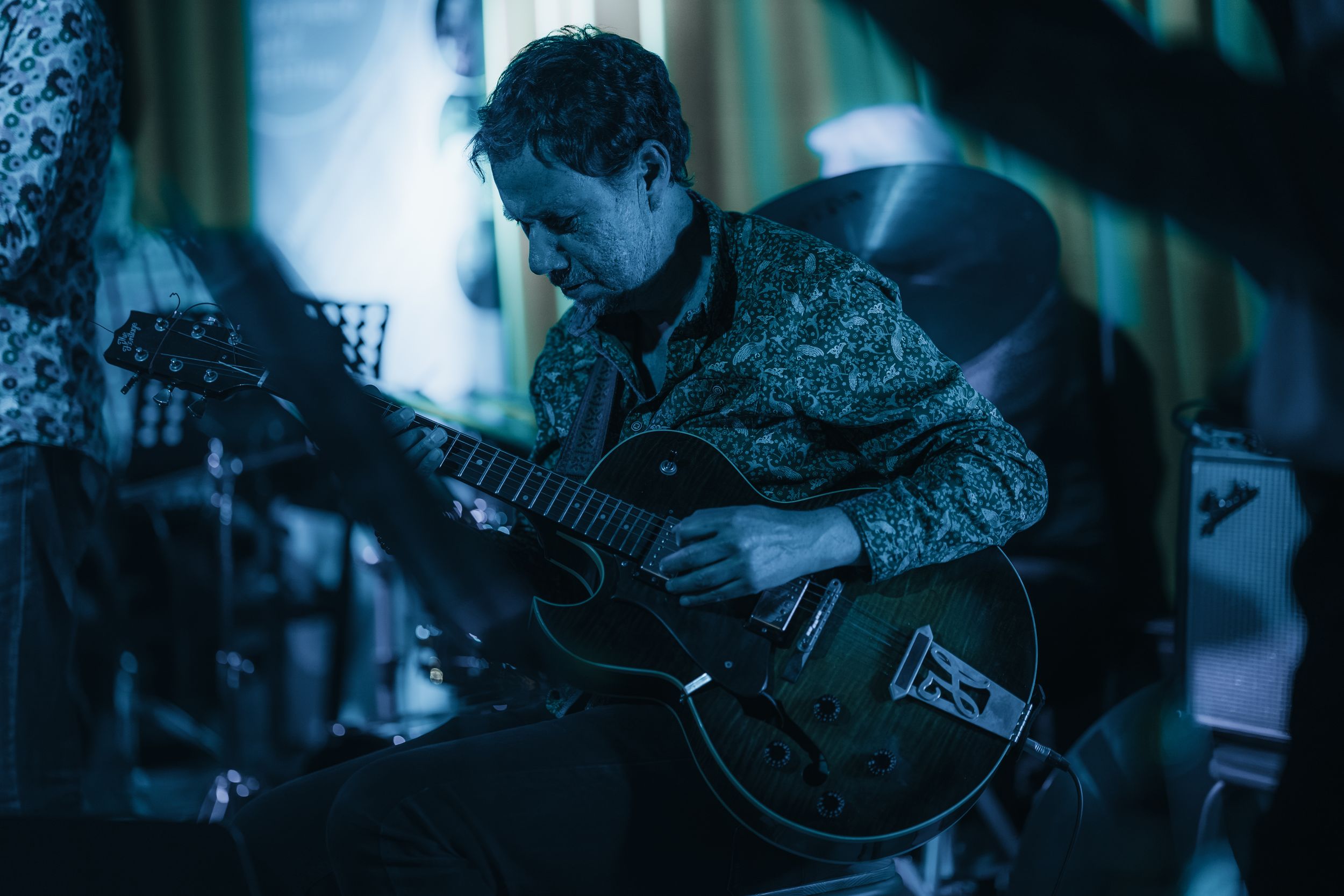 Musicians play instruments under cool blue theatrical lighting during live show.