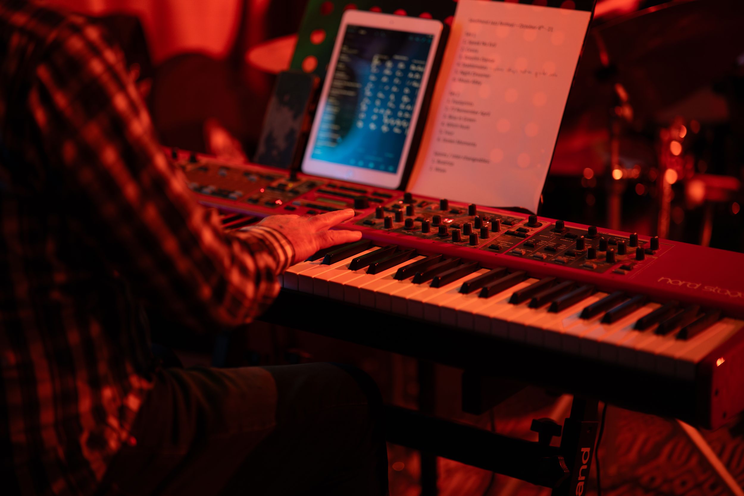 Musical equipment and keyboards illuminated by red stage lighting during performance.