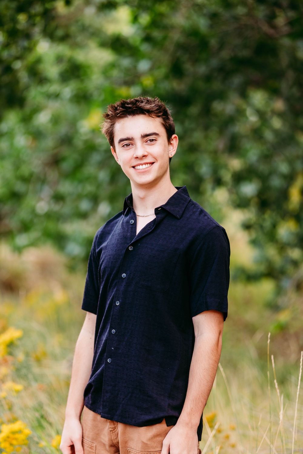 A young person in a navy polo shirt smiles at the camera in an outdoor setting with bokeh background.