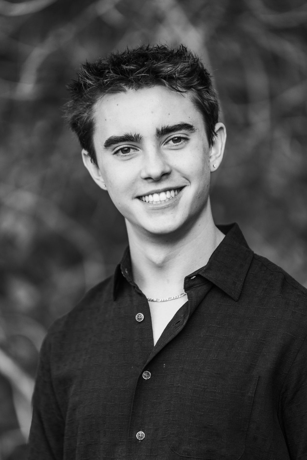 Black and white portrait of a young person in a dark button-down shirt smiling at the camera.