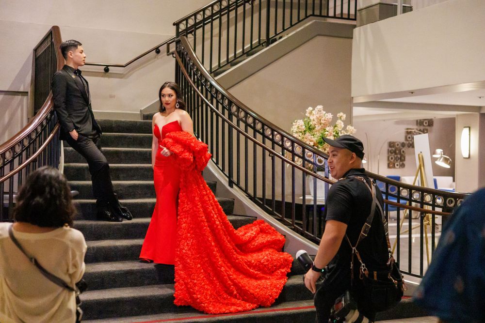 Photographer capturing a dramatic shot of a model in a flowing red gown on elegant staircase.