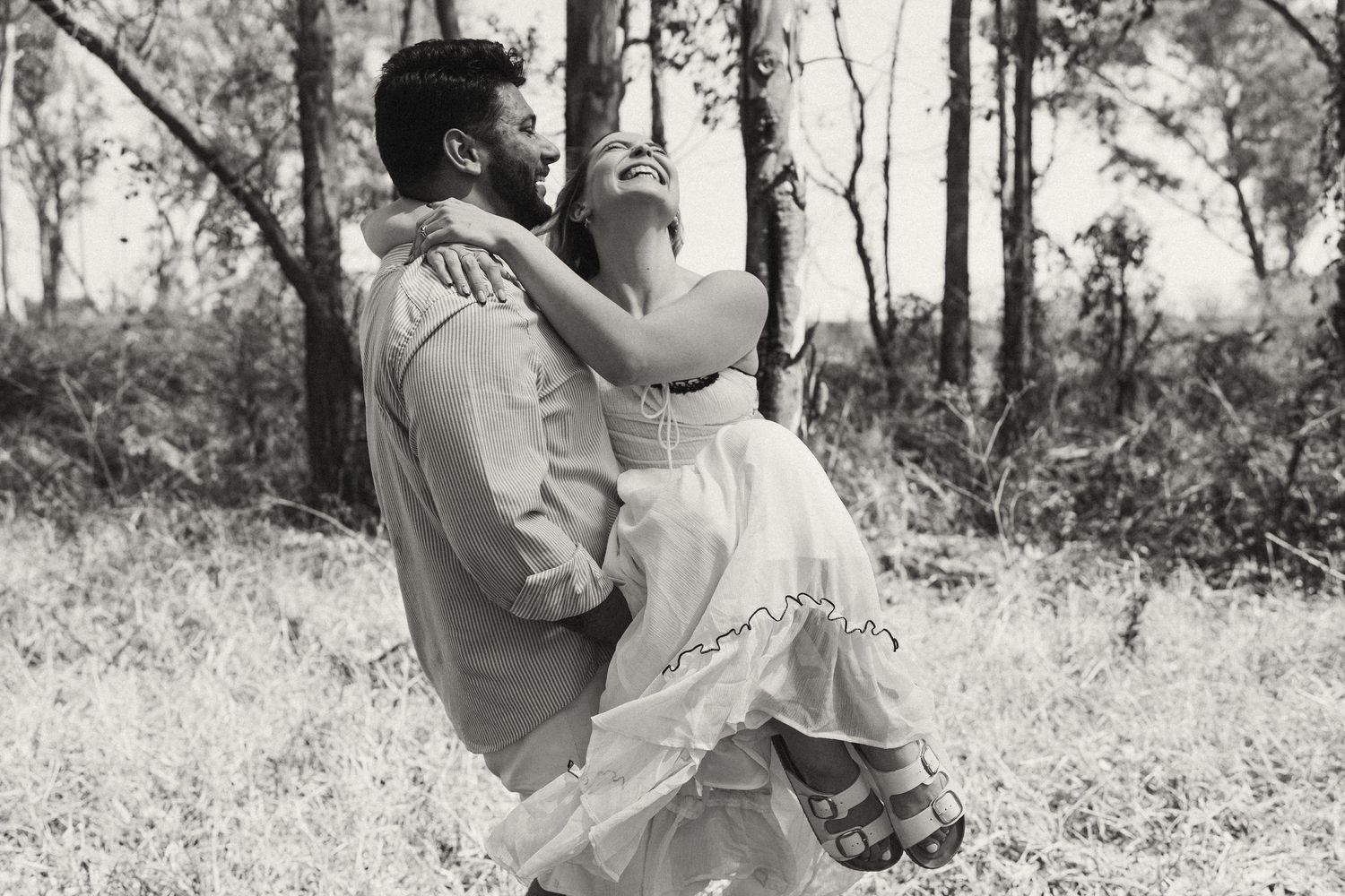 Couple shares tender moment in black and white photo amidst natural outdoor setting.