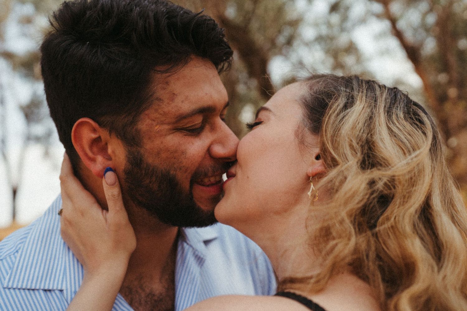 A romantic couple shares an intimate kiss outdoors with soft natural lighting.