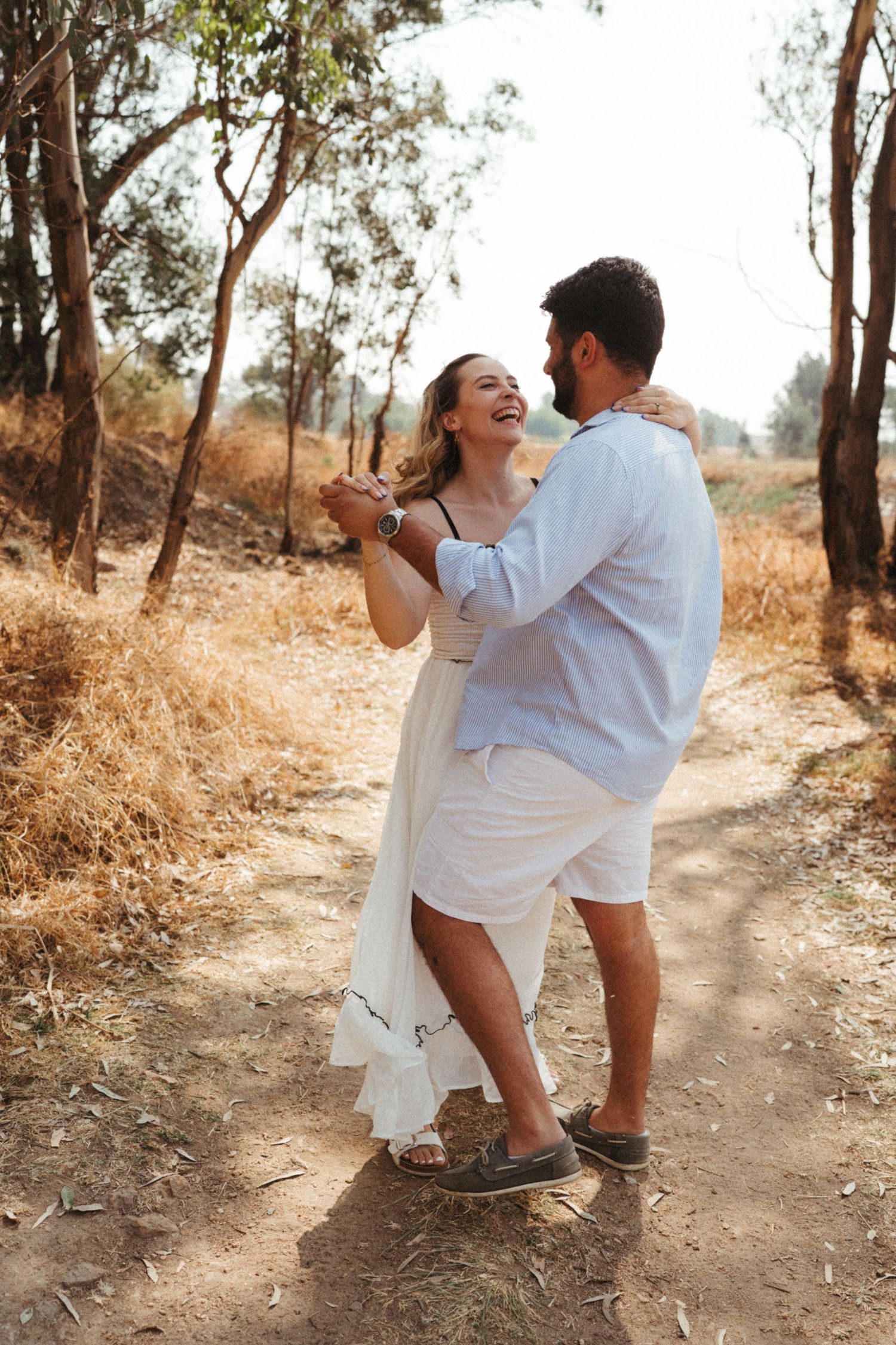 A joyful couple dances and laughs together on a sunny outdoor path.