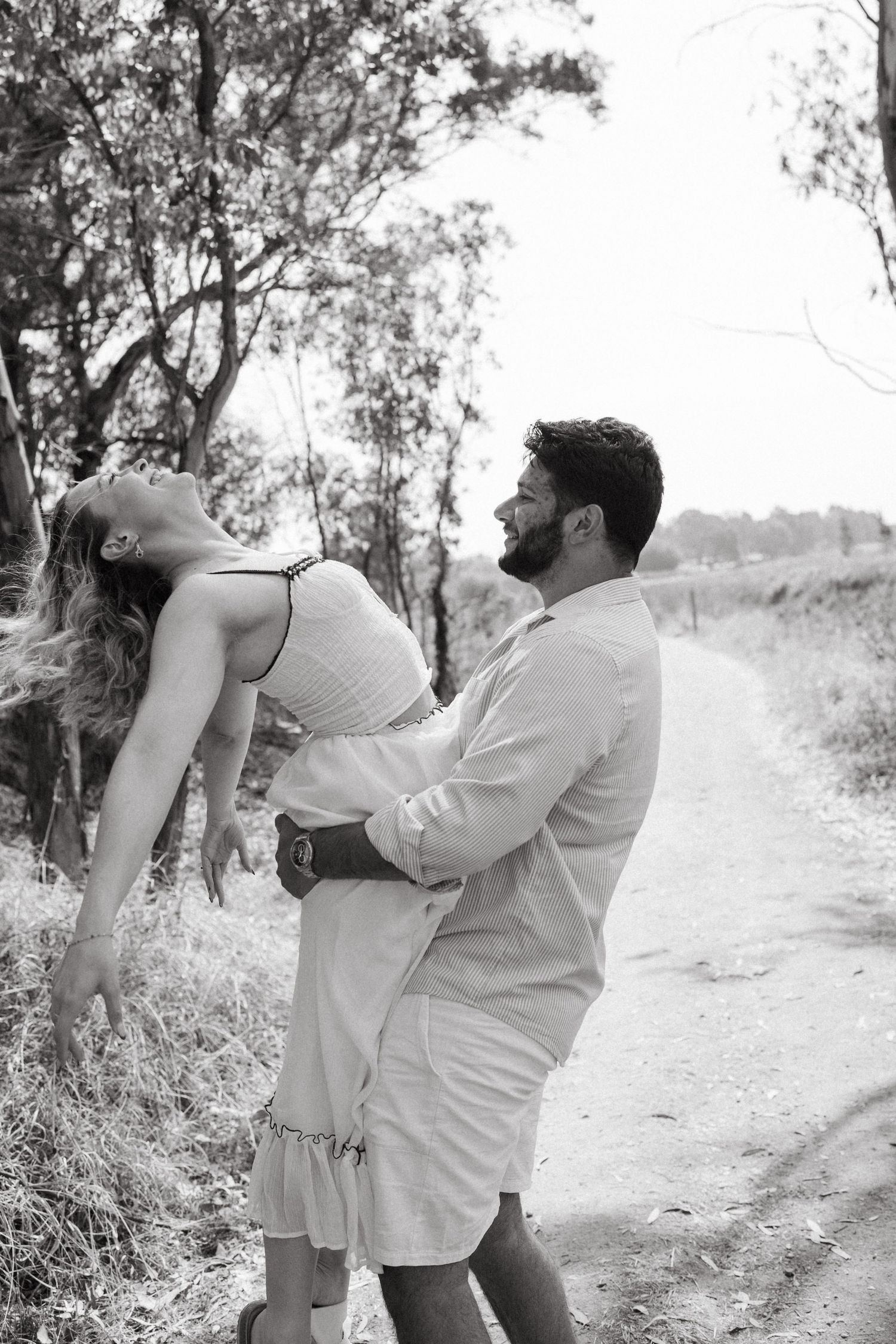 A couple shares a playful dip pose on a nature trail in black and white photography.