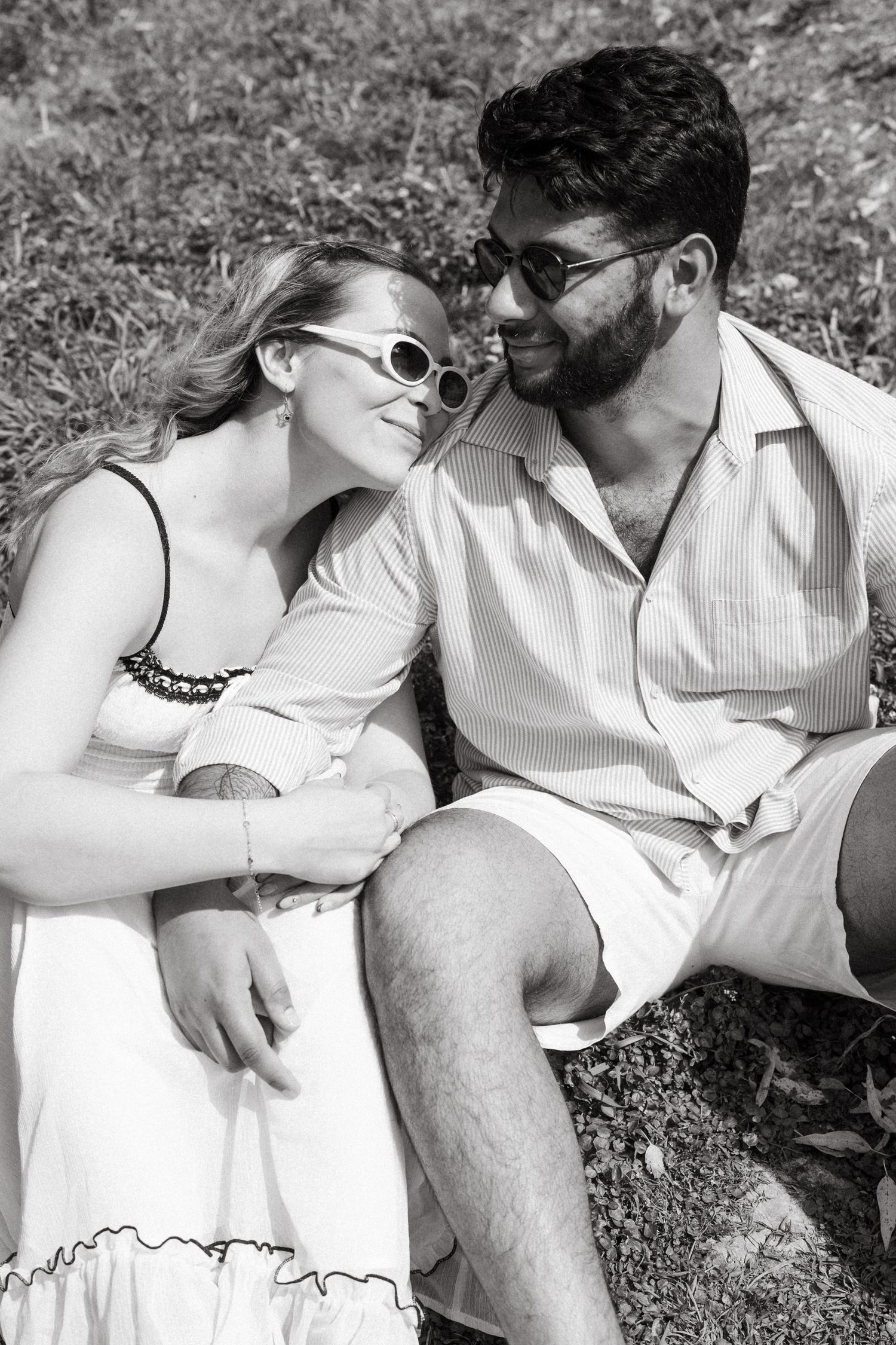 A couple wearing sunglasses shares an intimate moment while sitting outdoors.
