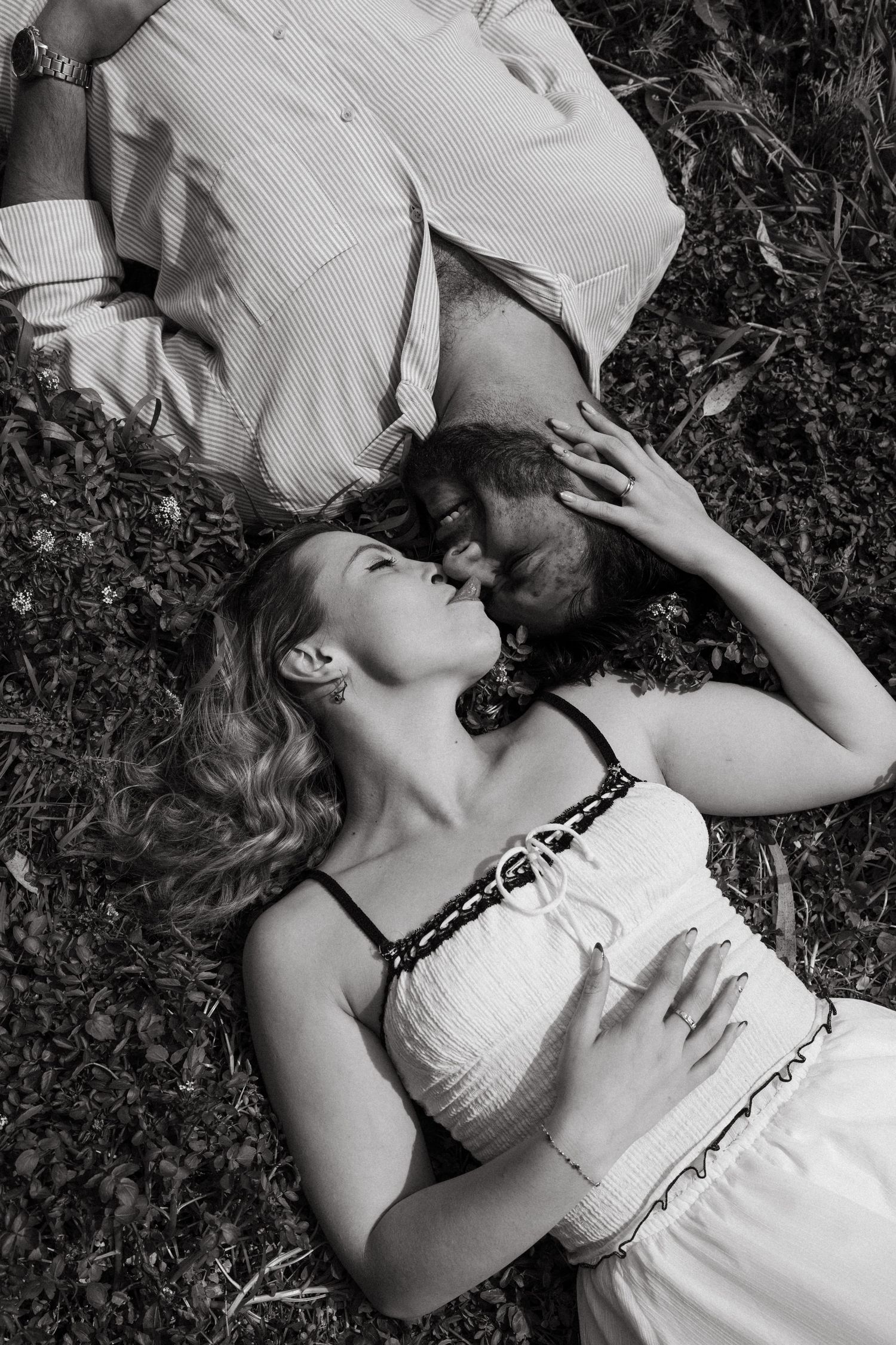 A romantic black and white photo of a couple lying in grass together.
