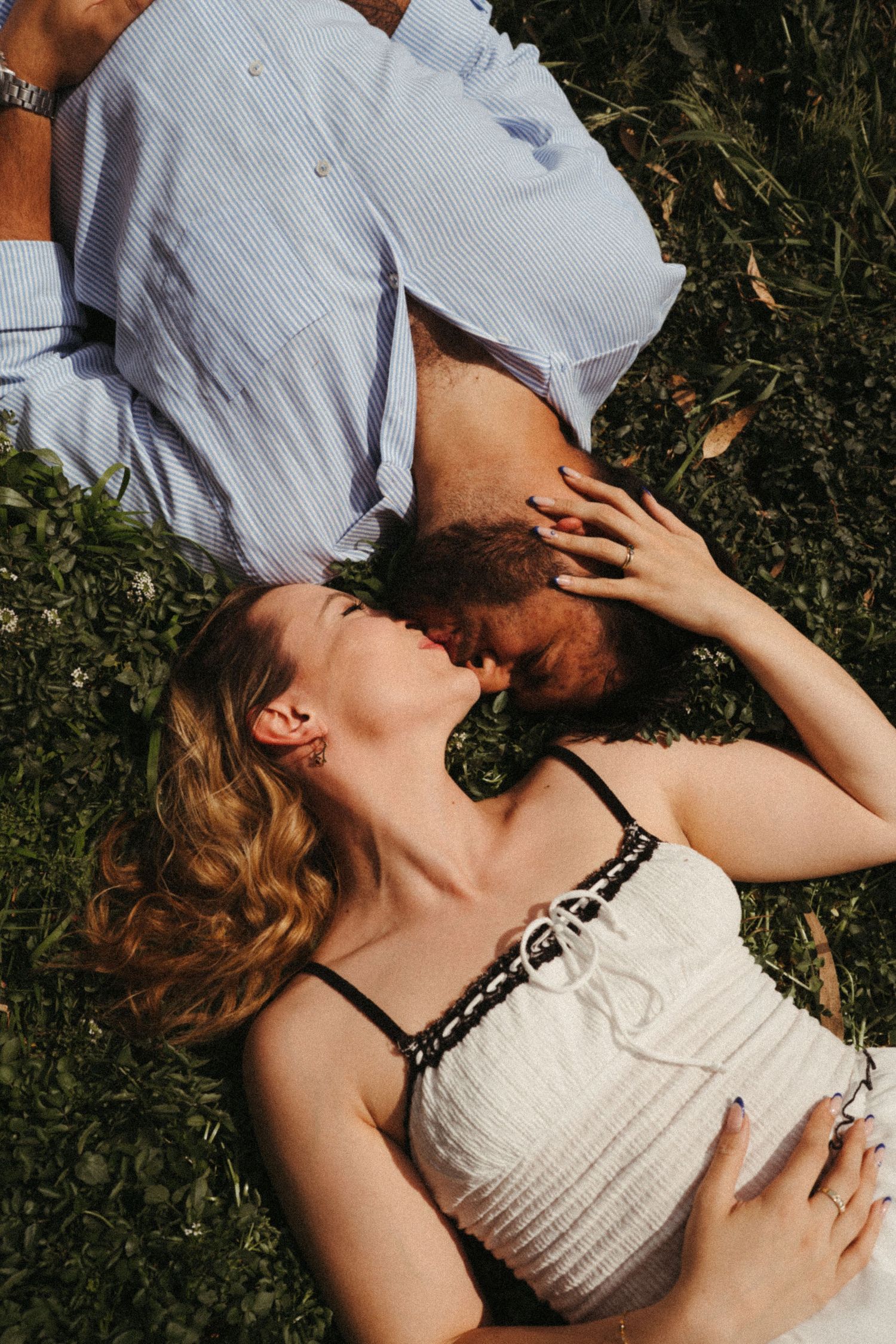 Intimate portrait of a couple lying on grass in summer sunlight.