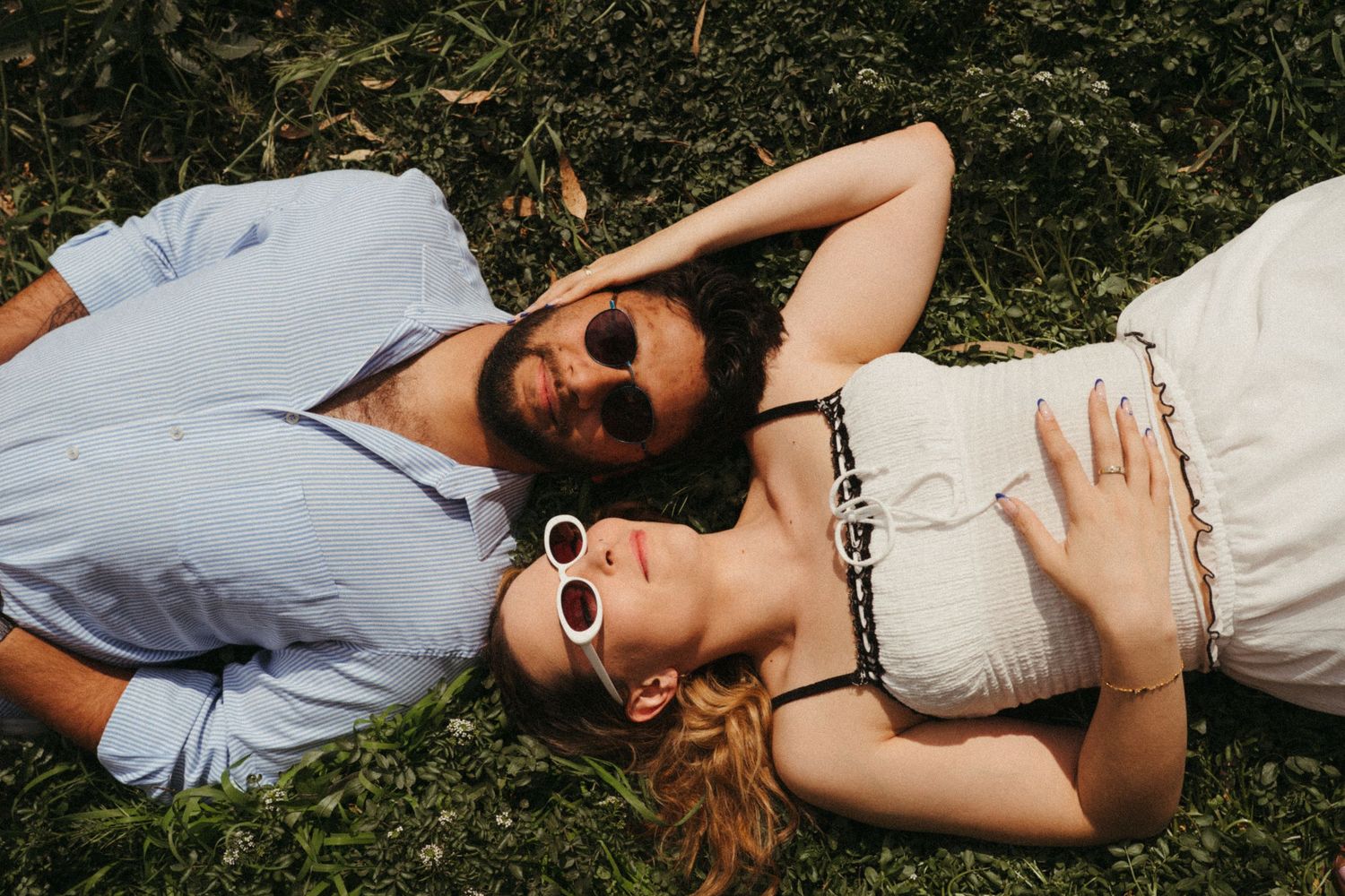 Couple wearing sunglasses lying on grass together on a sunny day.