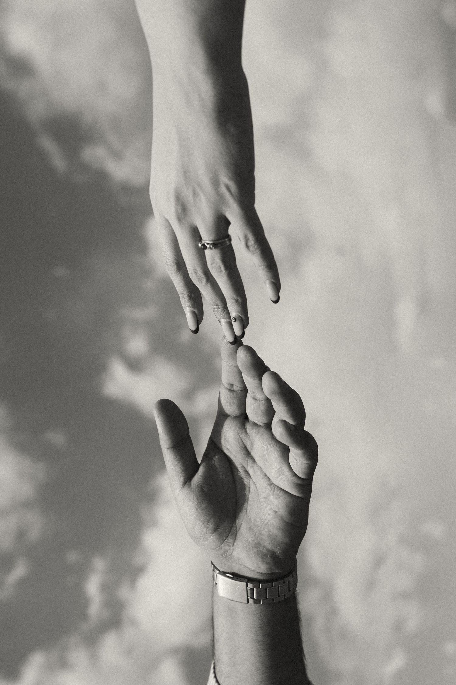 Artistic black and white photo of two hands reaching towards each other.
