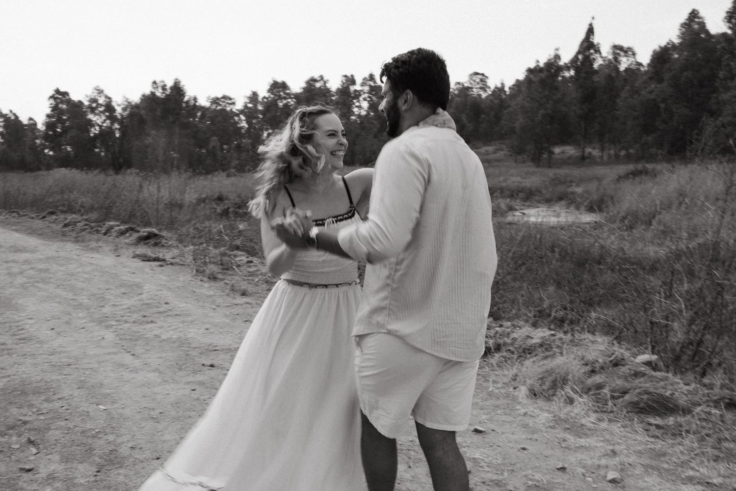 Black and white photo of a couple sharing a tender moment on a country road.