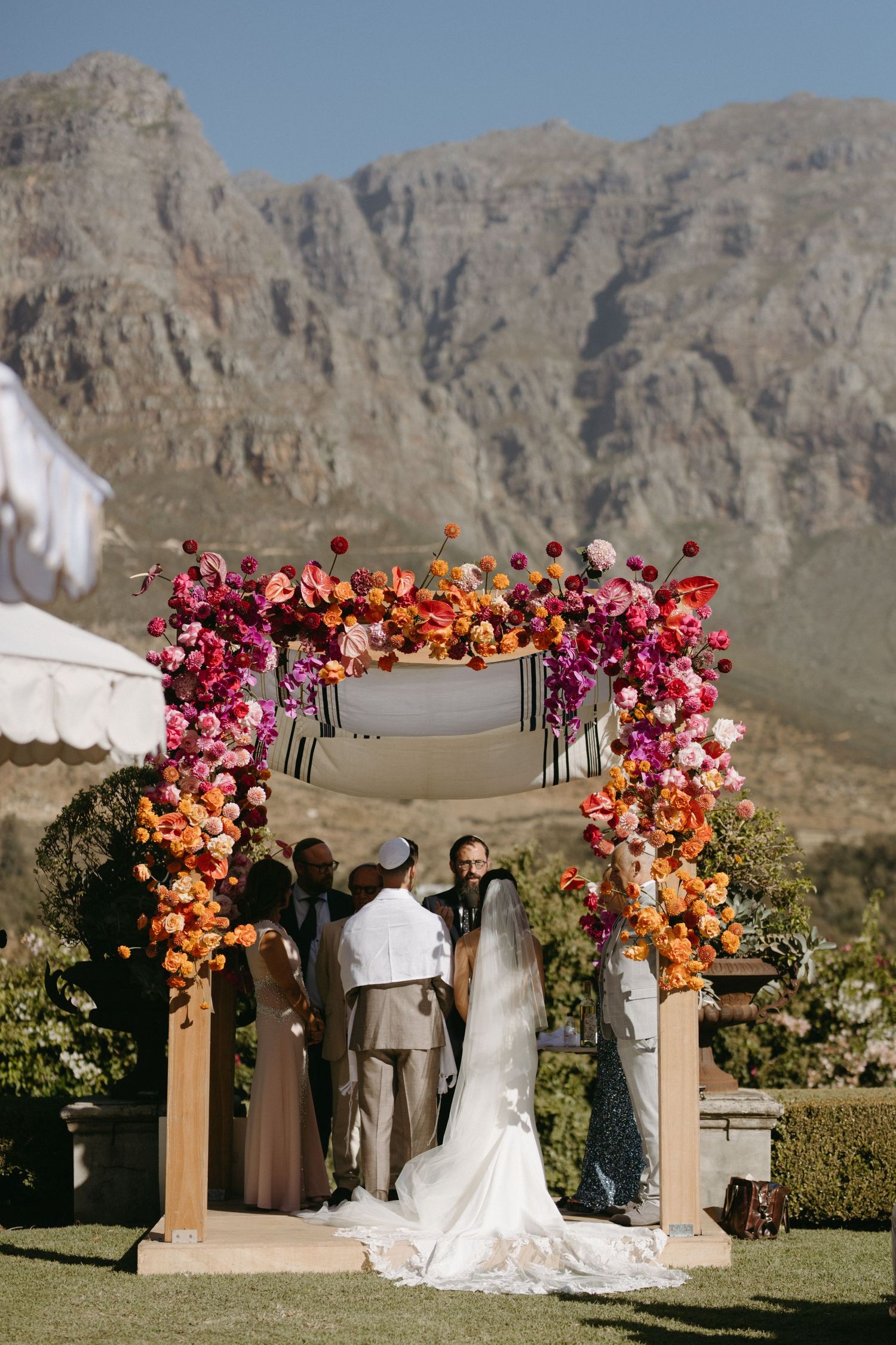 Outdoor wedding ceremony under floral arch with mountain vista backdrop.