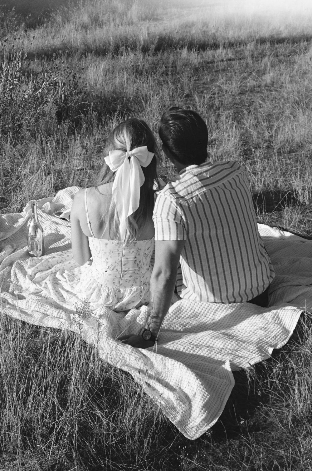 Black and white sequence of figures relaxing on blankets in a grassy field.