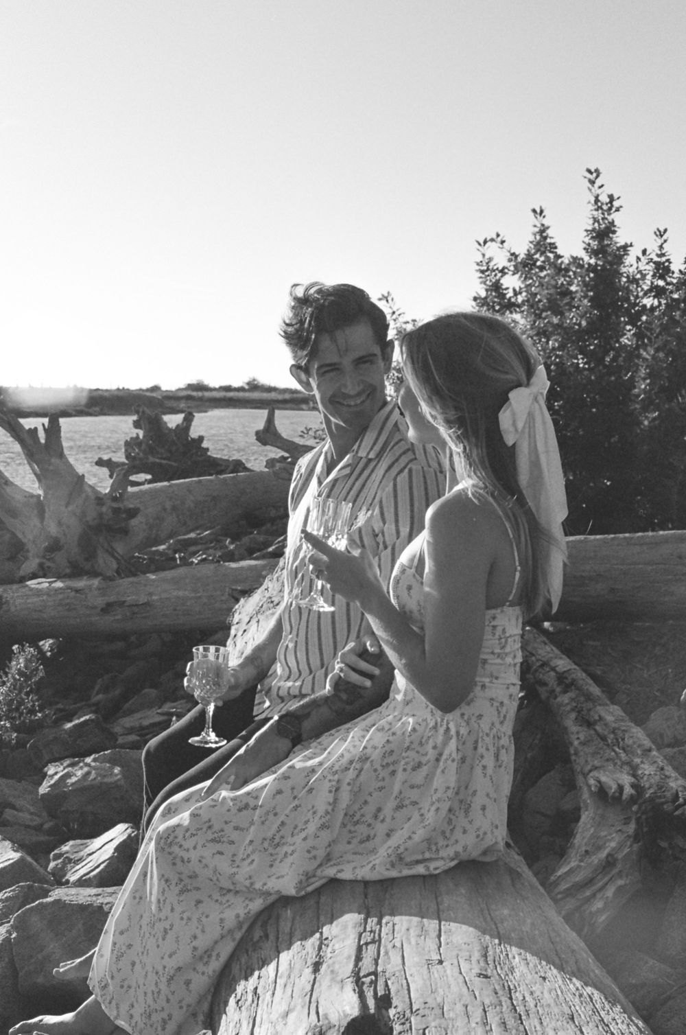 A couple sits together on a fallen log in vintage black and white photographs.