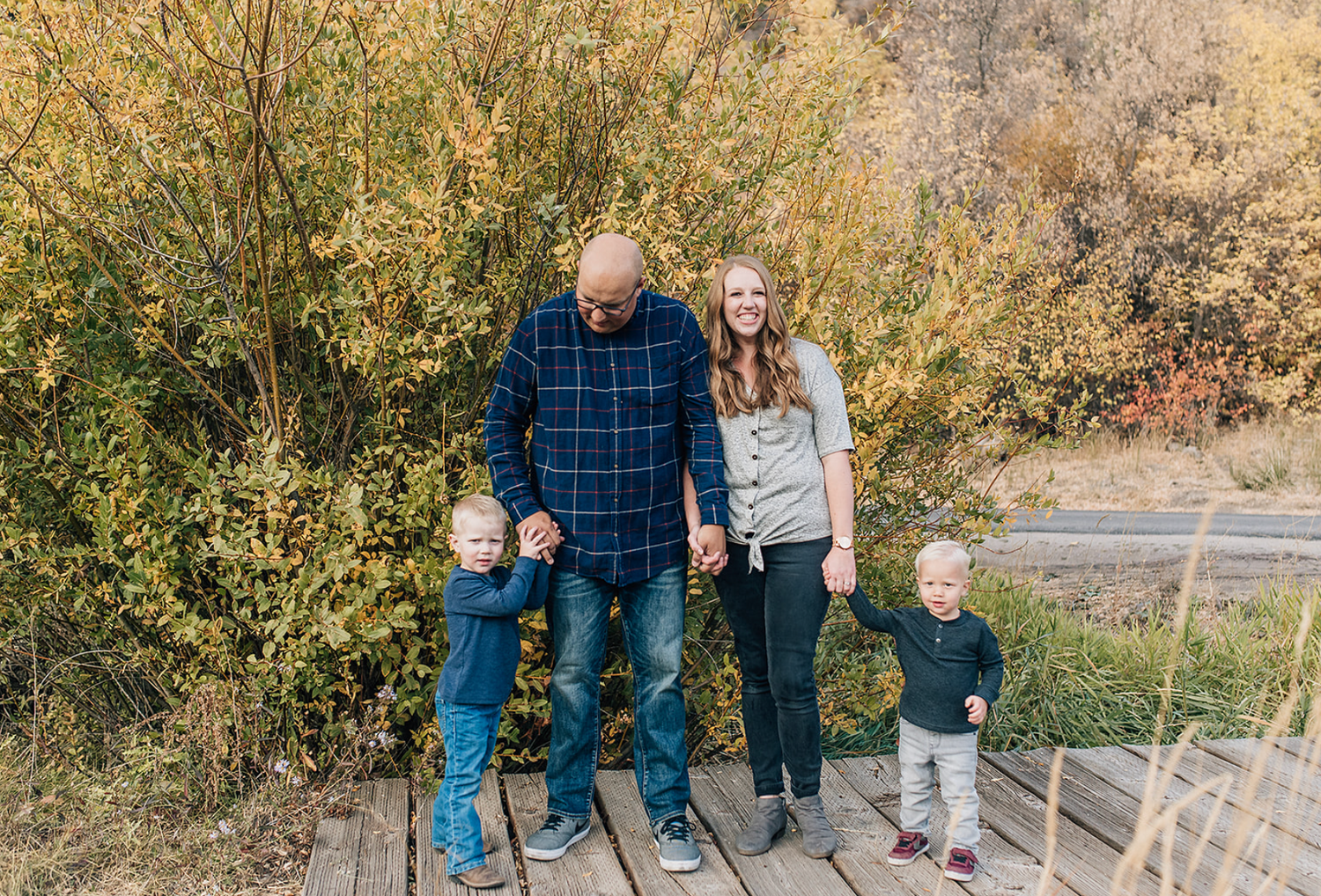 Family standing together on wooden boardwalk surrounded by fall foliage.