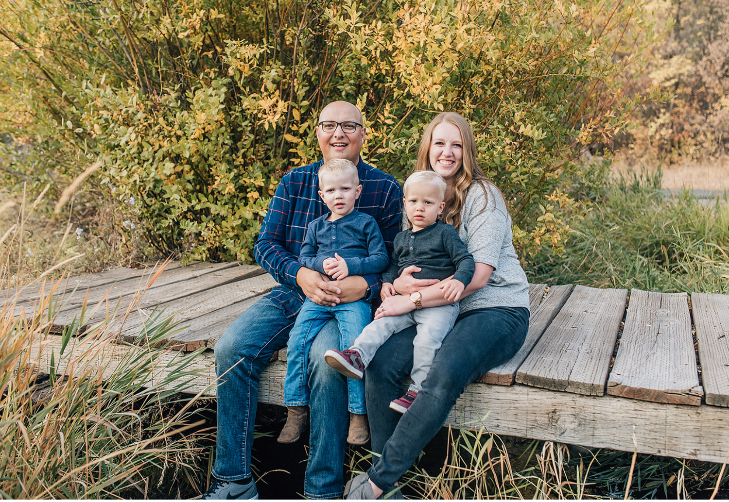 Family sitting together on wooden deck surrounded by autumn foliage.