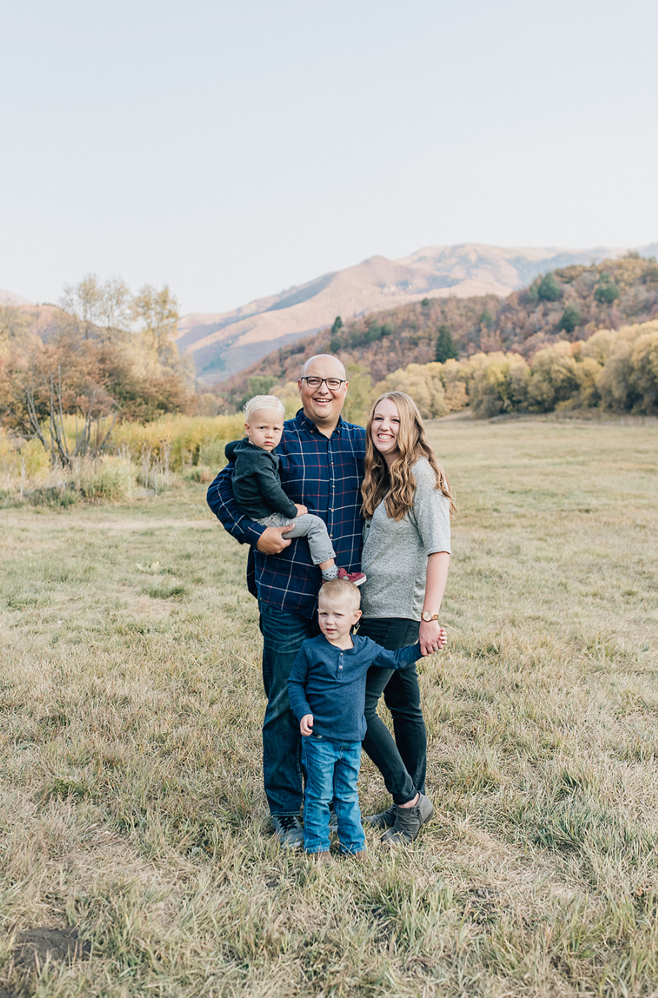 Autumn family portrait in a grassy field with mountain backdrop.
