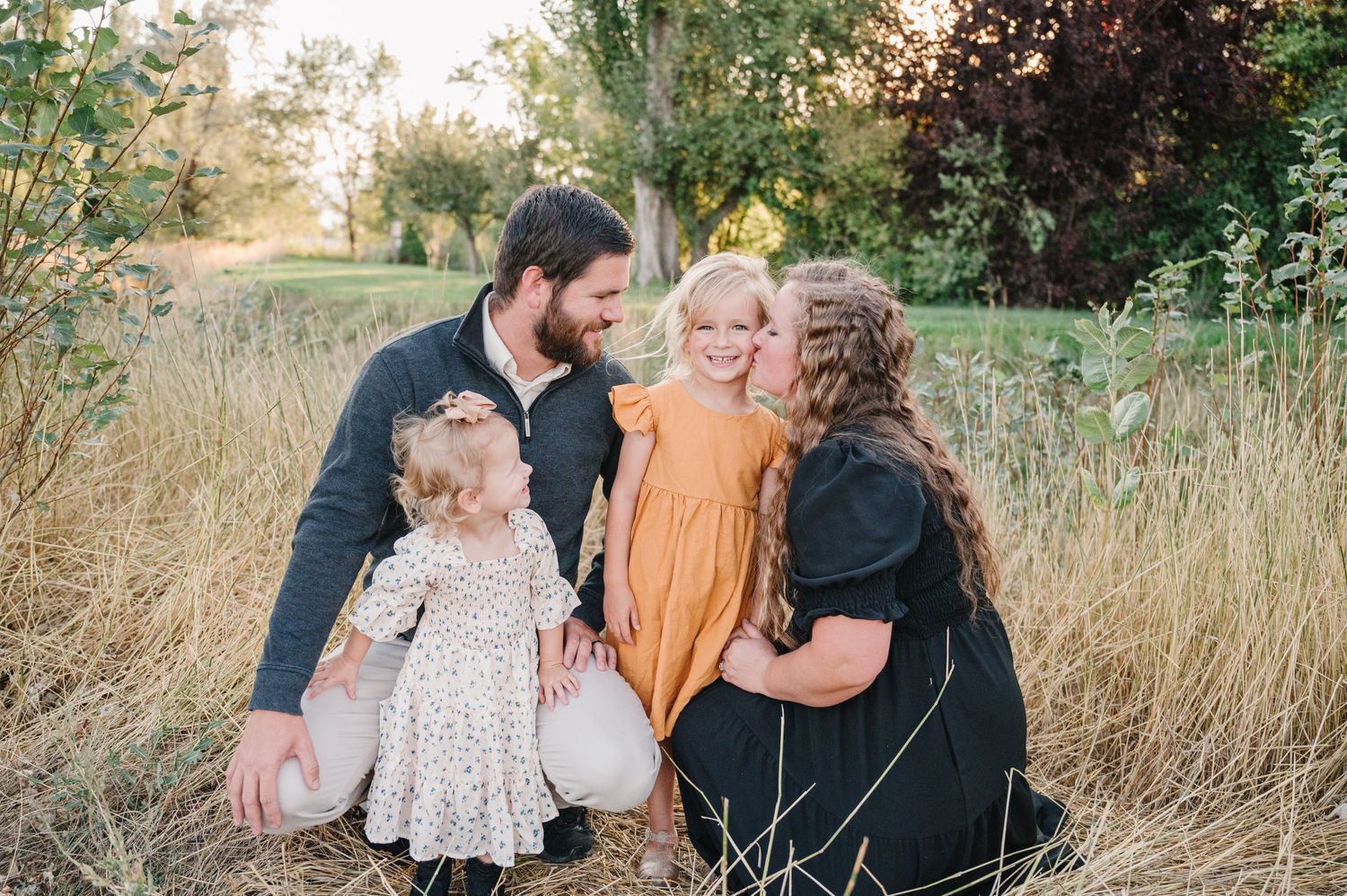 A family embraces together in a field of tall grass during golden hour.