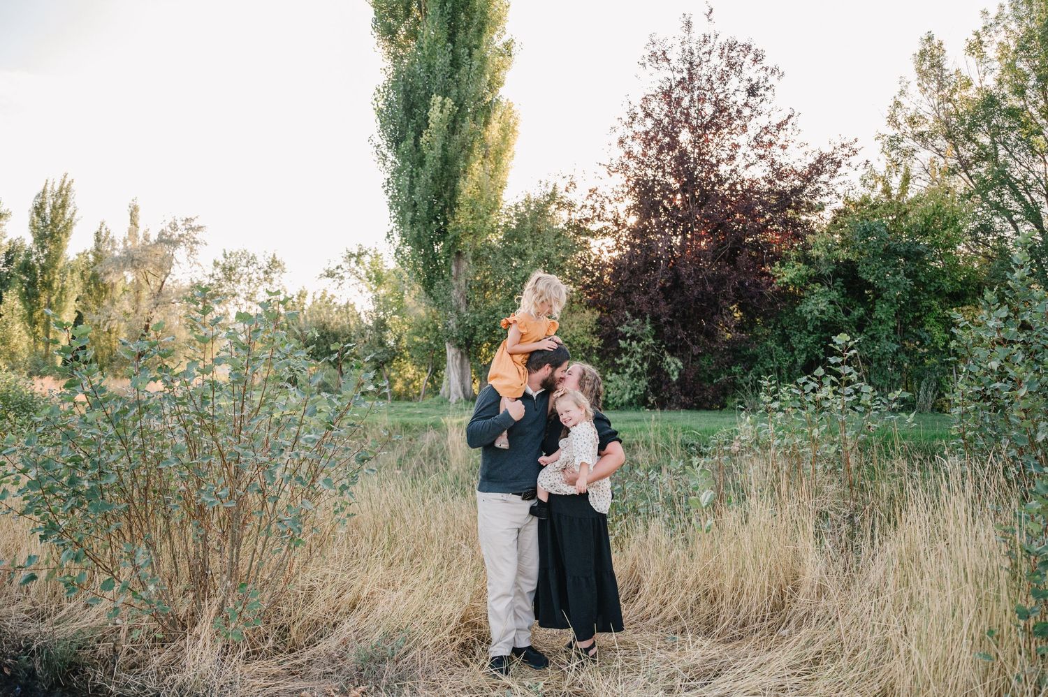 A couple shares a tender moment while standing in tall grass at sunset.