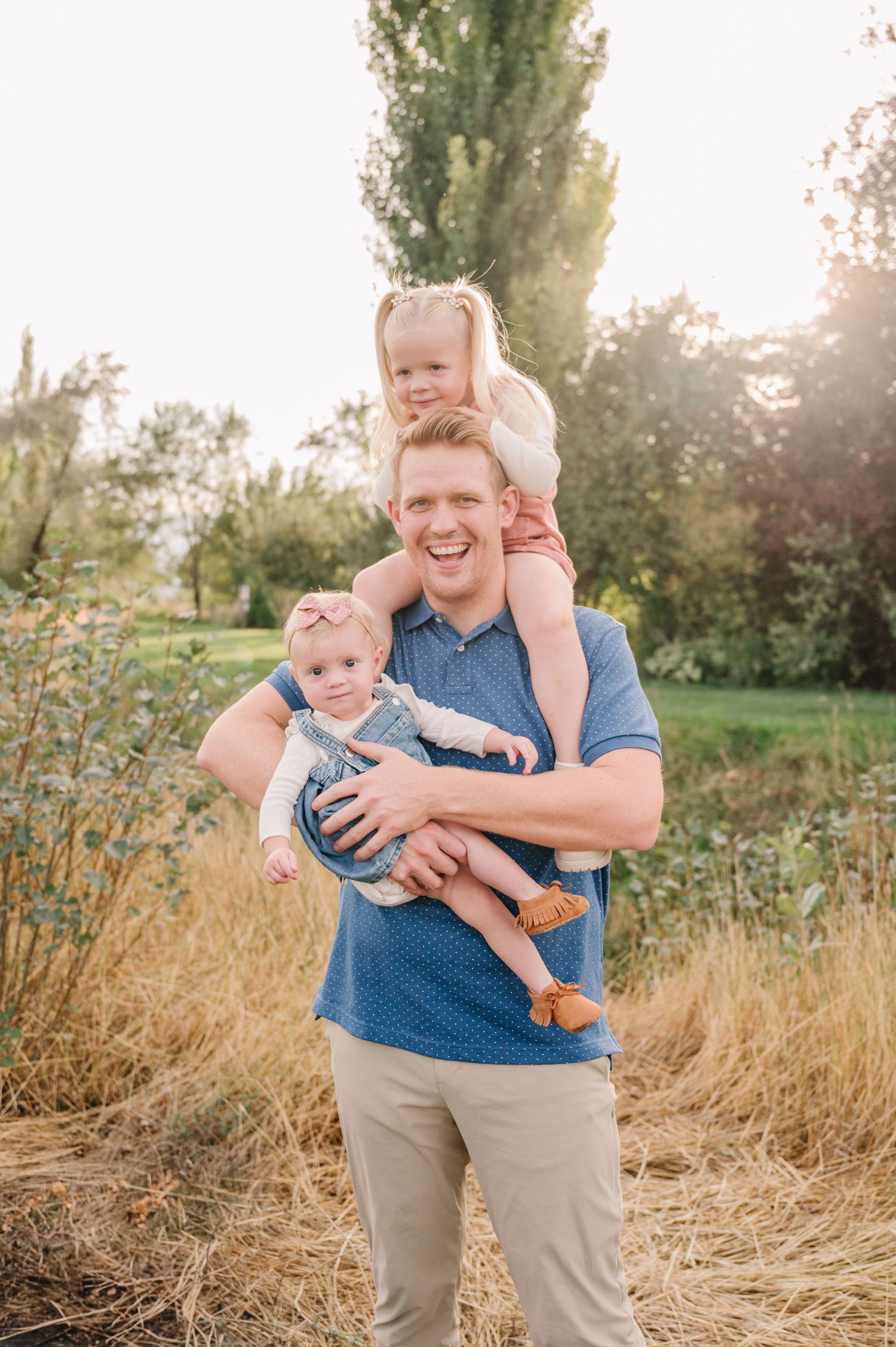 A playful moment captured outdoors as little ones are carried in golden sunlight.