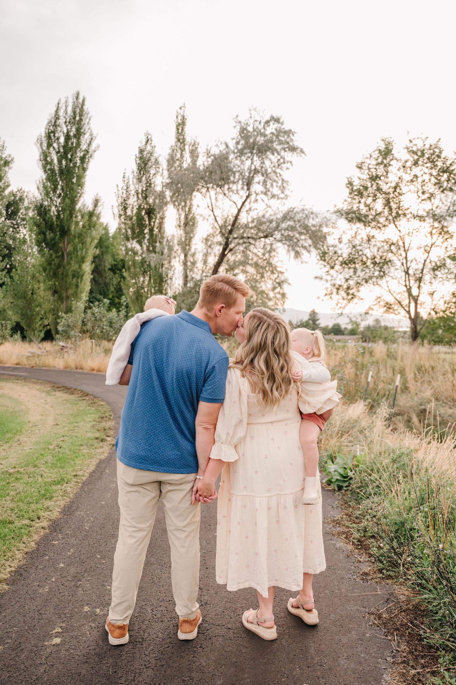 A couple shares an intimate moment while walking on a path surrounded by tall grass at sunset.