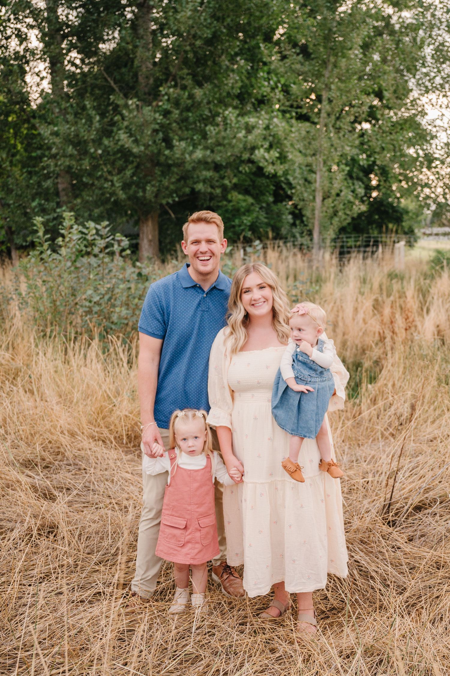 A family poses together in a field of golden grass during sunset.