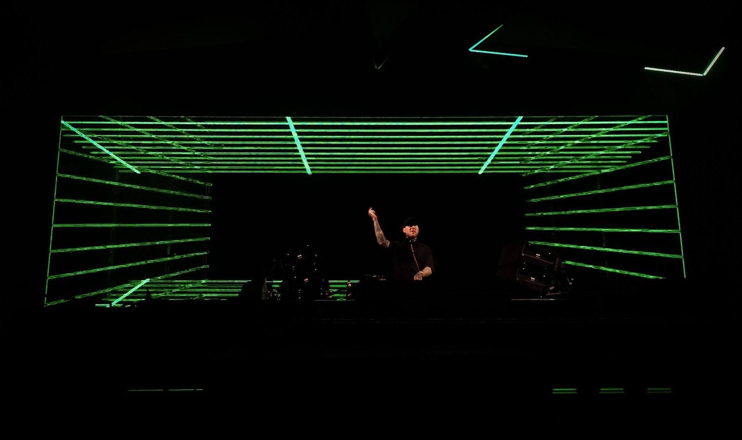 A person performing or standing on a stage in a dark club setting with geometric green laser lighting. dj parookaville concert techno,trance