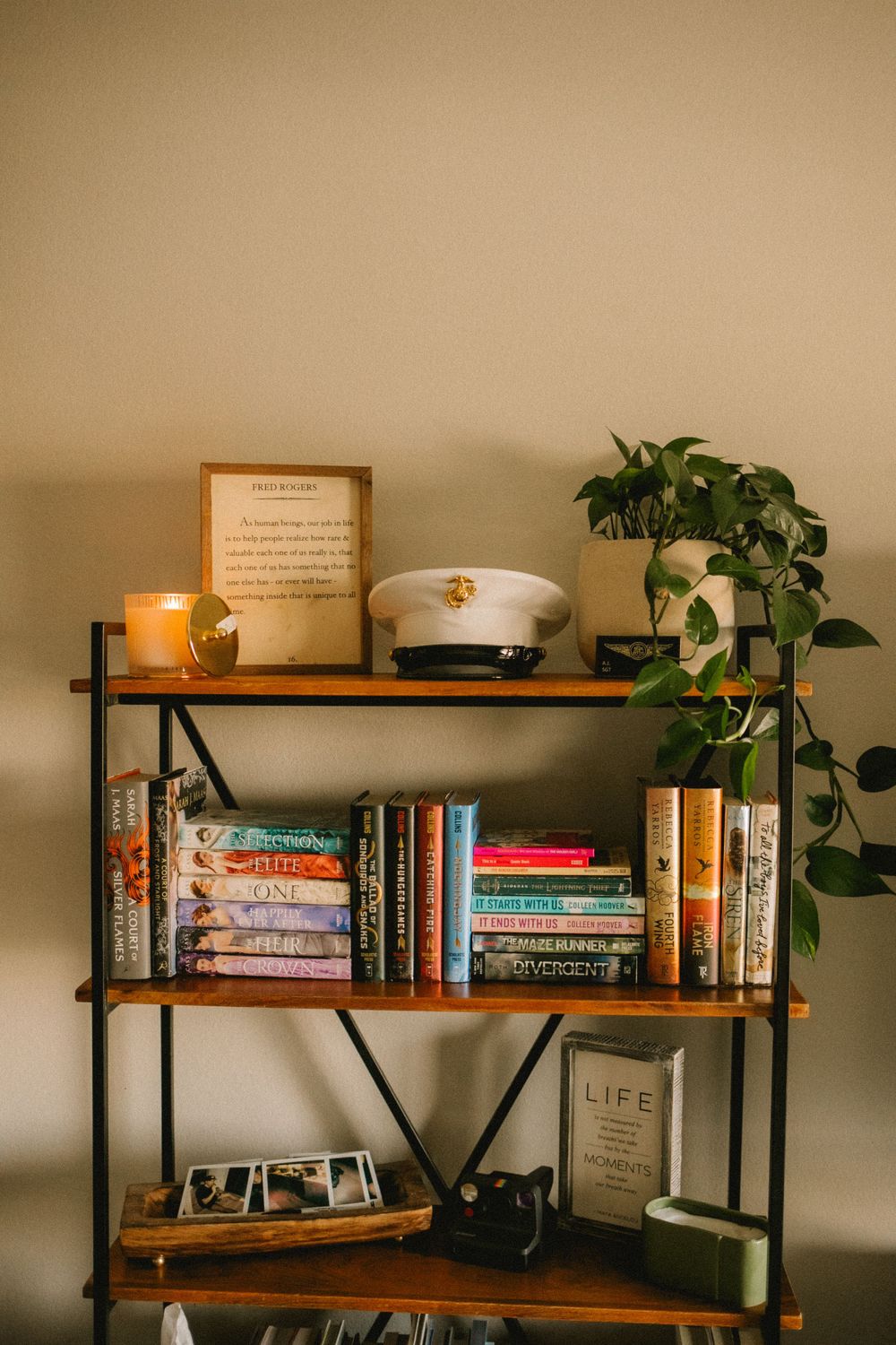 Wooden bookshelf with books, military cap, framed art, candle, and trailing pothos plant.