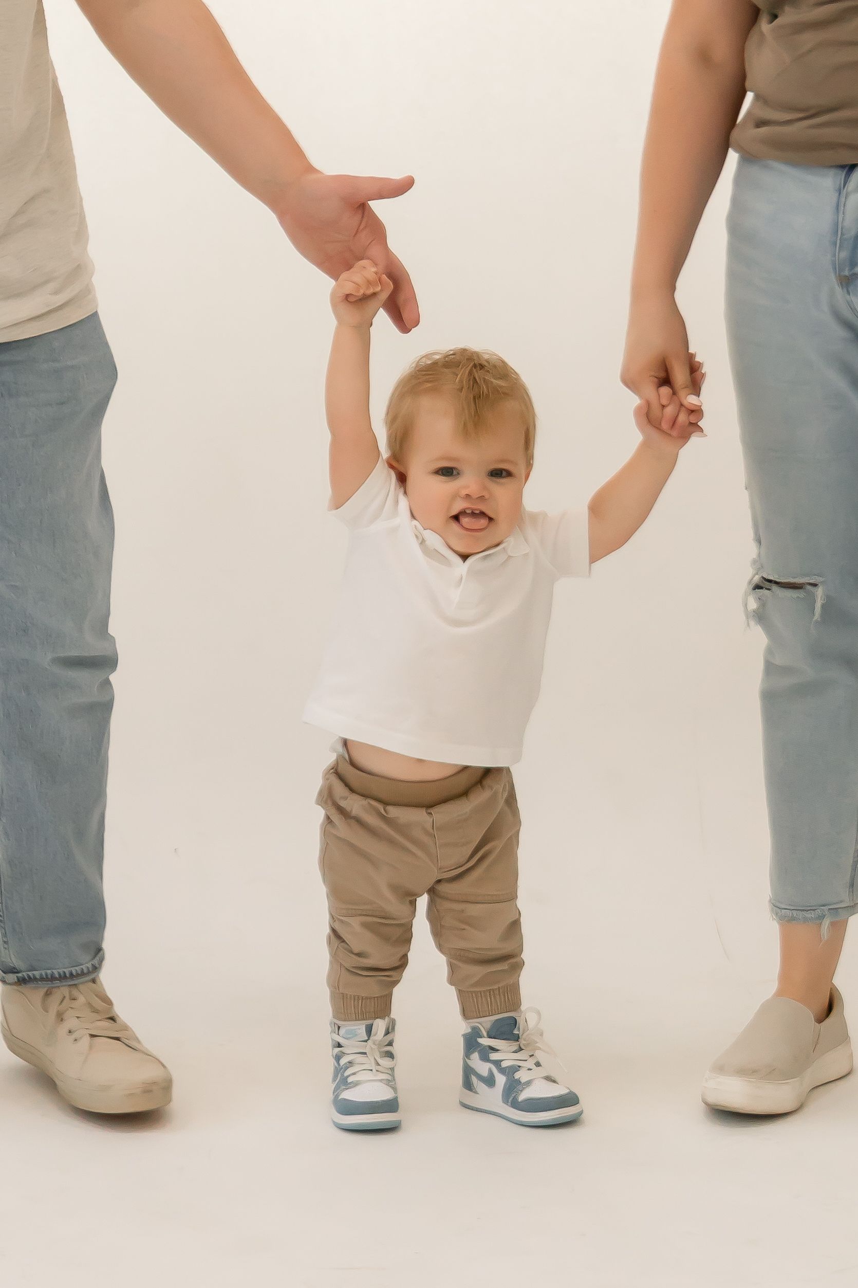 Little boy holding his parent's hands and learning to walk in cute photo.