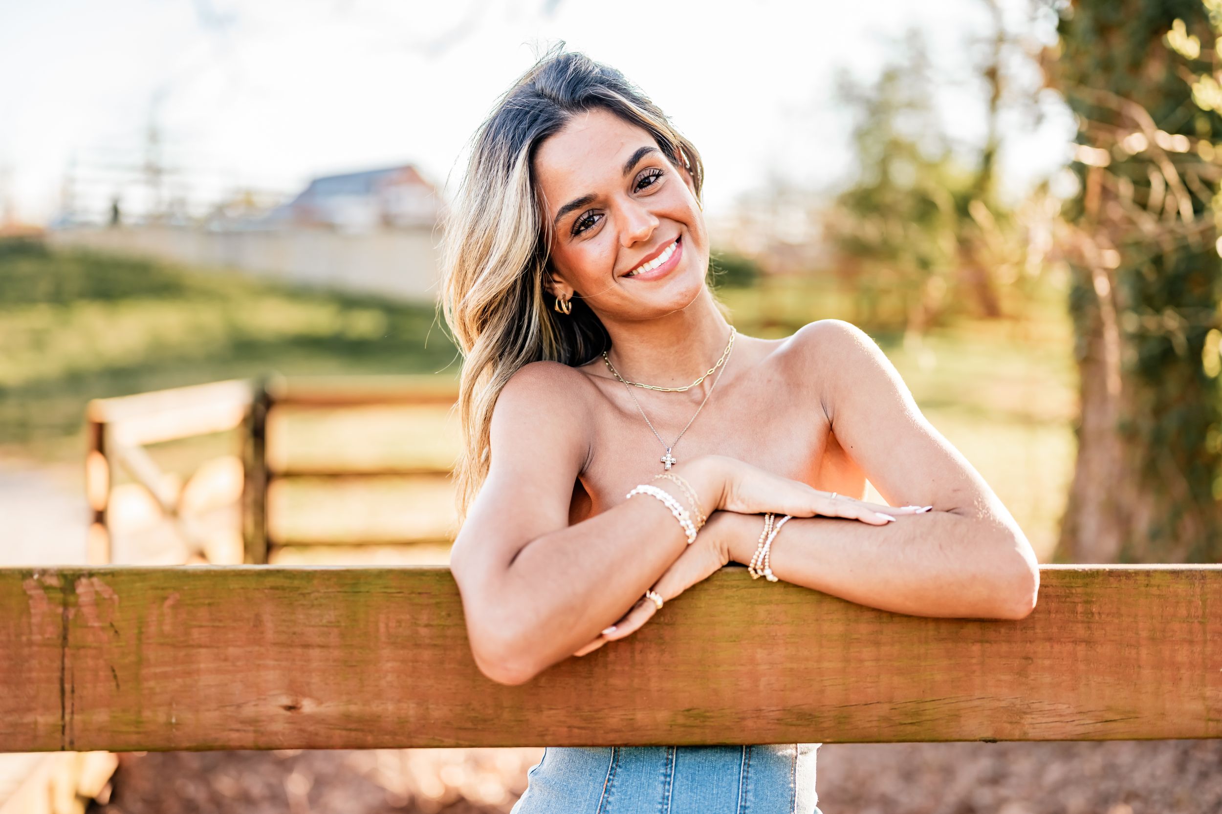 Woman in floral dress poses near wooden fence during golden hour sunset for outdoor portrait photography series.