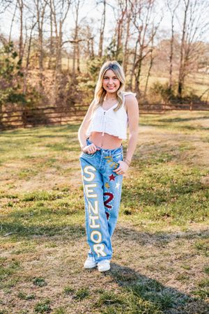 High School Senior Casual spring outfit features embroidered jeans with floral details and a white crop top in an outdoor natural setting.