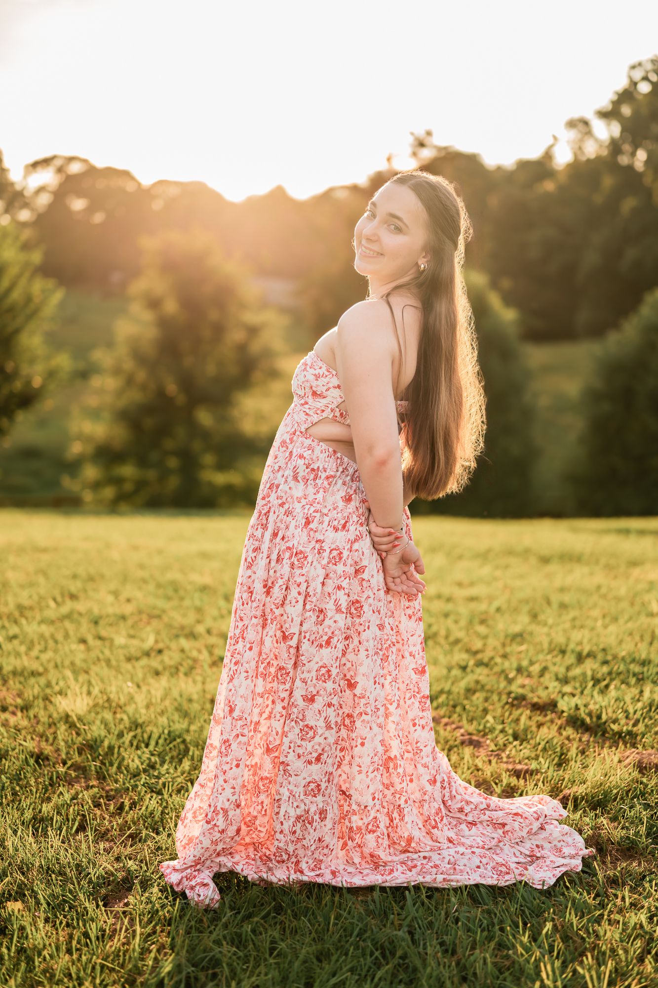 Person in a floral pink dress sits gracefully in a sunlit meadow at golden hour.