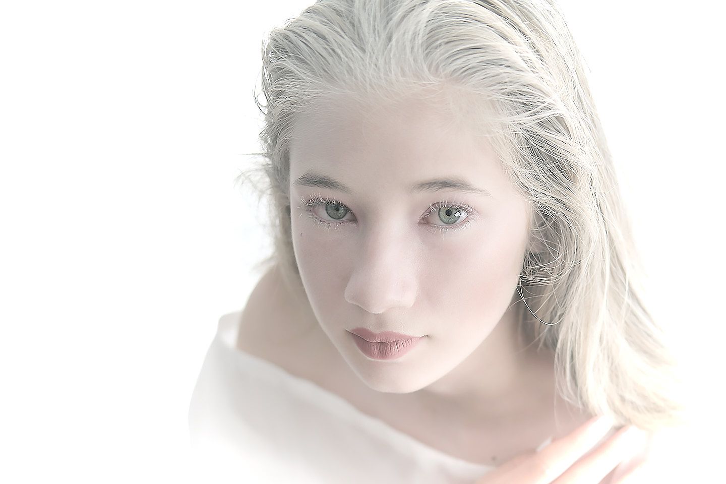 Retrato etéreo de joven con cabello plateado y ojos verdes en fondo blanco