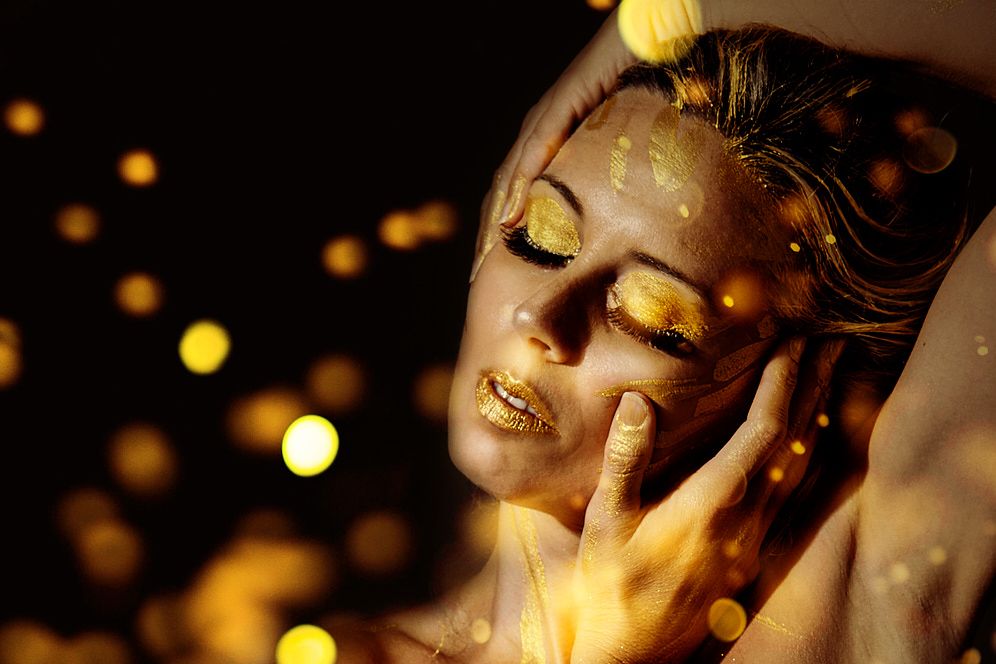 retrato de fantasia de una mujer con maquillaje dorado envuelta en reflejos de oro