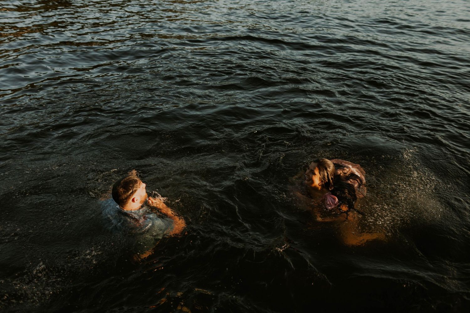 Two people swimming and enjoying golden hour light reflecting on dark ocean waters.