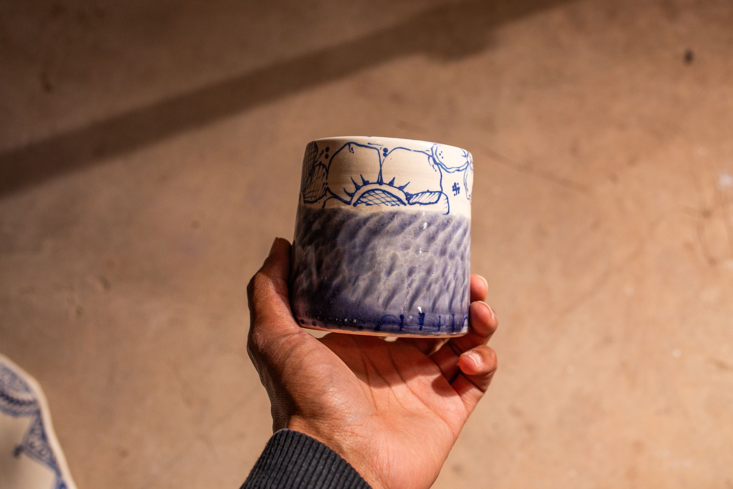 Hand holding a decorative blue and white ceramic cup with floral patterns in natural light.
