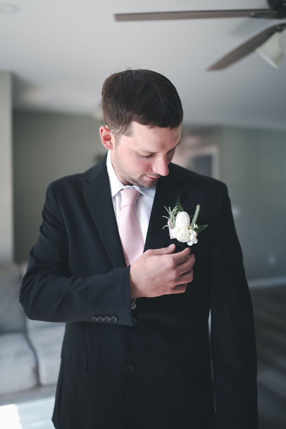 A person in black suit and pink tie adjusts their white boutonniere.
