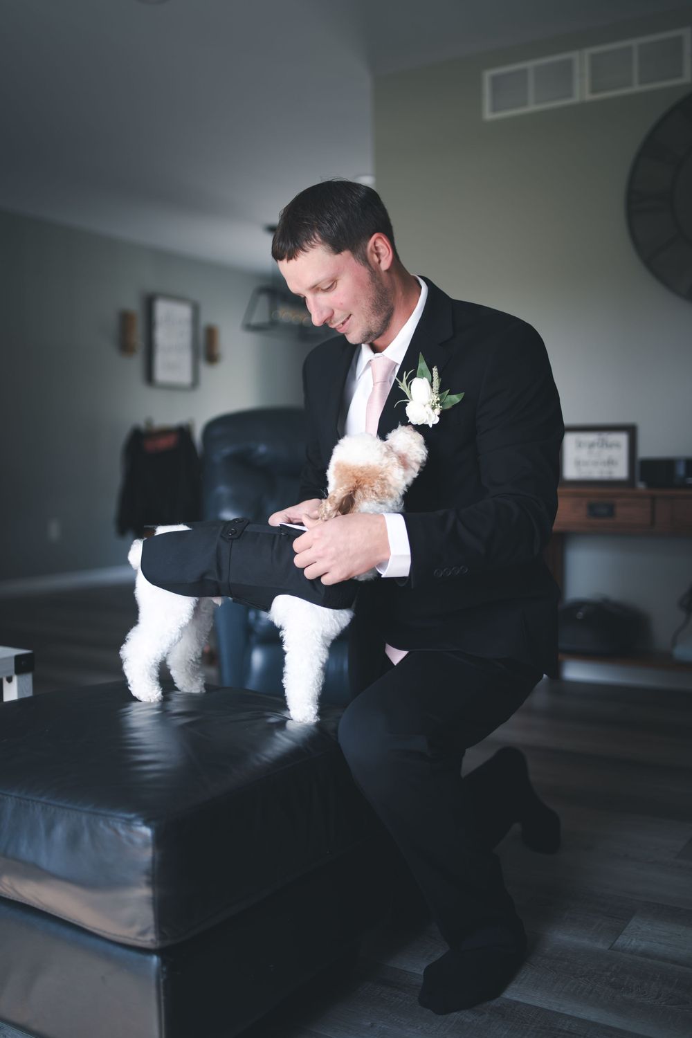Person in formal attire interacts with small white dog during wedding preparations.