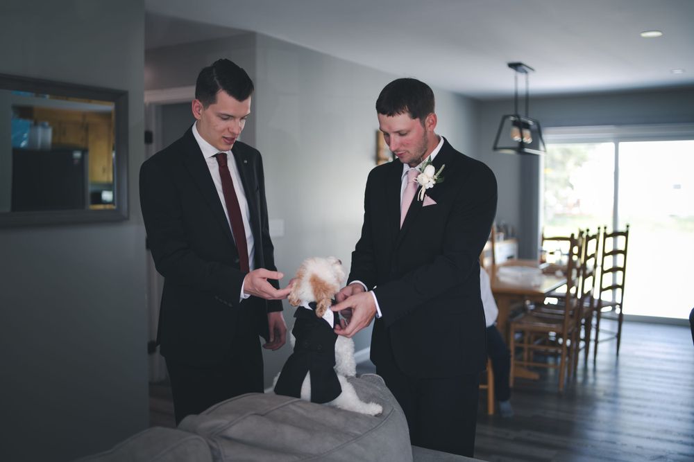 Two groomsmen in formal suits getting ready before a wedding ceremony while discussing details.