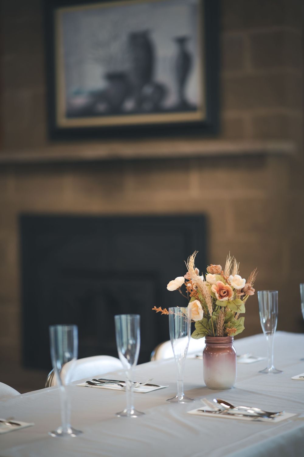 An elegant table setting with blurred artwork and fireplace in background.