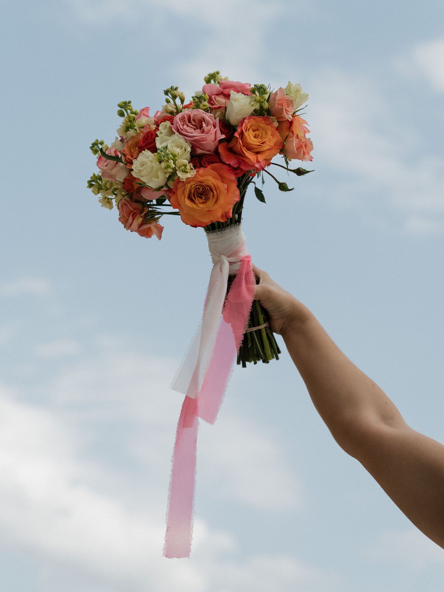 Still life with disco ball, heart-shaped sunglasses, perfume bottle and pink and white floral arrangement against white tulle.