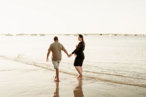 Couple walking hand in hand along beach shoreline at sunset.