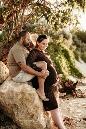 Couple sitting on coastal rocks during golden hour, sharing an intimate moment.