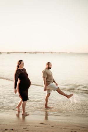 Two people playing and splashing in shallow beach water during golden hour.