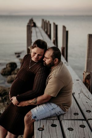 Couple sharing tender moment on wooden pier at dusk overlooking calm waters.